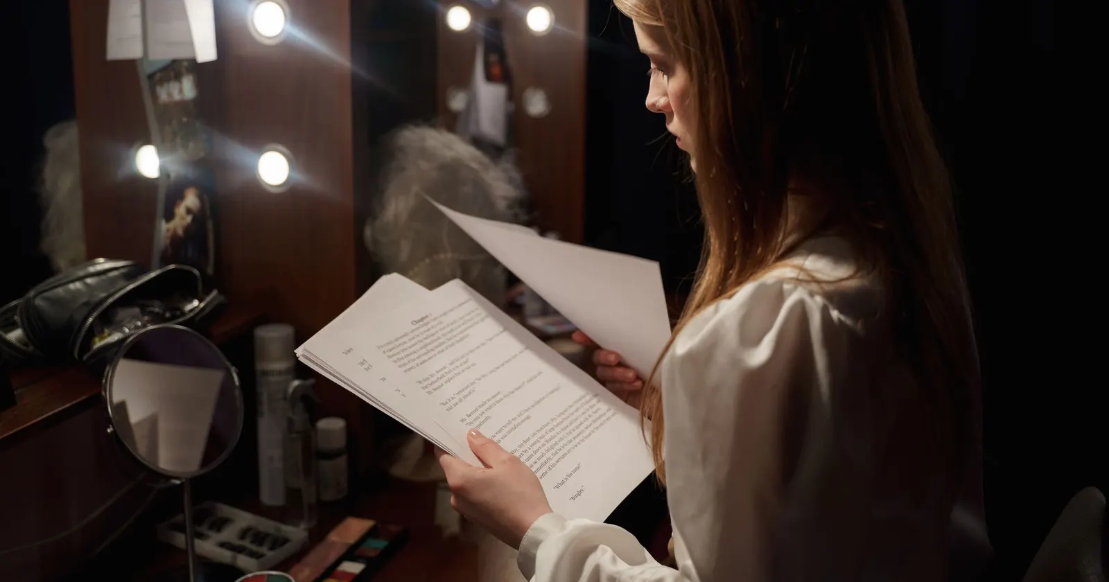 Une comédienne lit son texte dans une loge, devant un miroir bordé d'ampoules