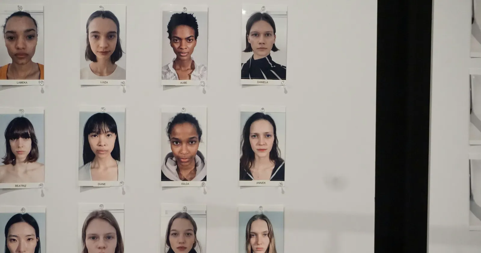 Un mur de portraits épinglés en rangées, chacun avec un prénom imprimé dessous, dans les coulisses d'un casting